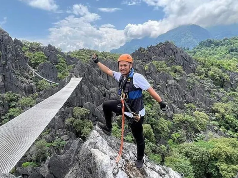 Travelers exploring a high suspension bridge in a dramatic Laos mountain landscape.