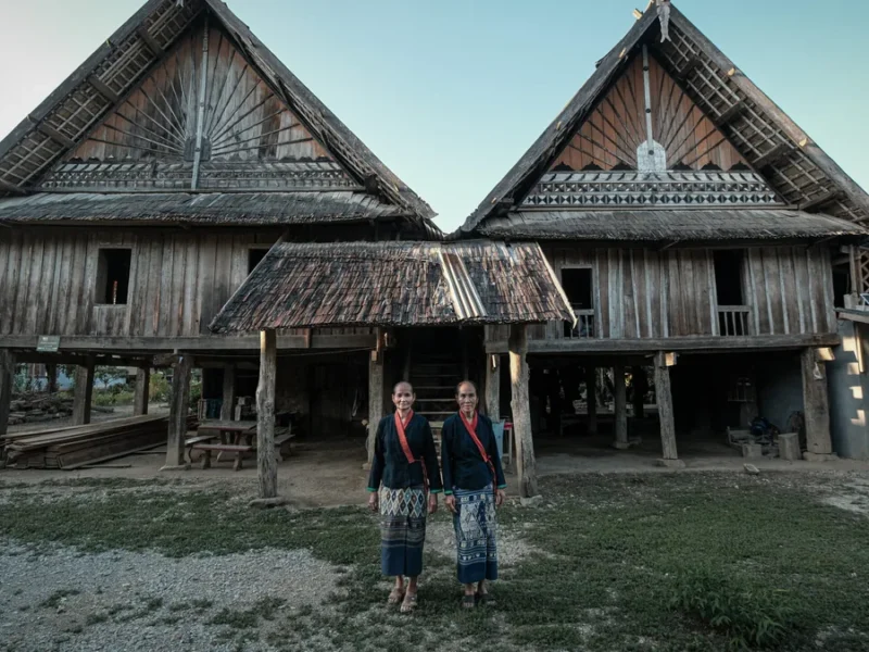 Travelers visiting traditional wooden homes in Laos during a cultural homestay journey.