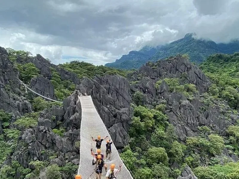 Traveler crossing a suspension bridge in a lush Laos mountain landscape on an adventure journey.