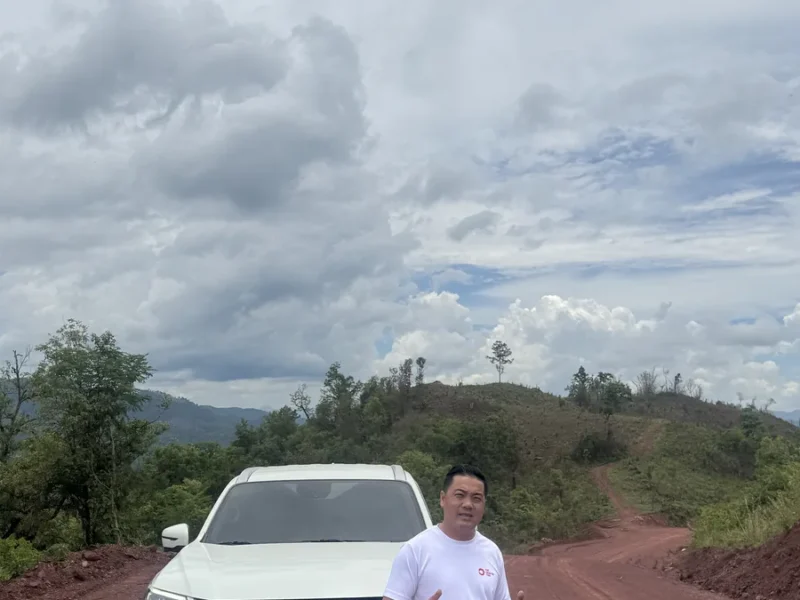 Traveler beside a four-wheel-drive vehicle on a remote Laos road during an overland expedition.